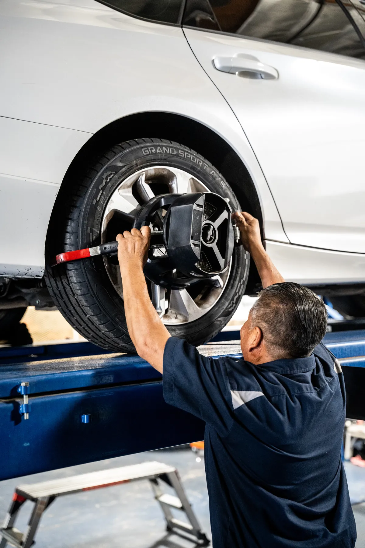 Technician clamping an alignment head onto the front wheel of a car on the alignment rack