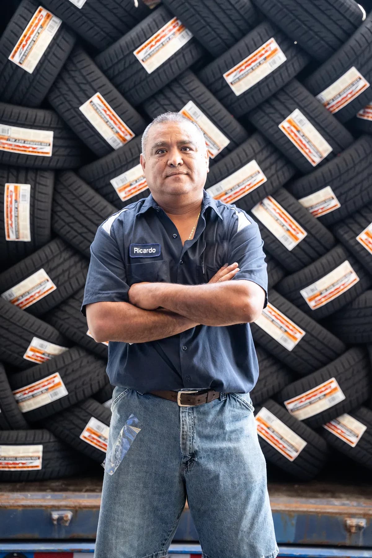 Ricardo from the Kwik Tire crew, arms crossed in front of a container stacked with new tires