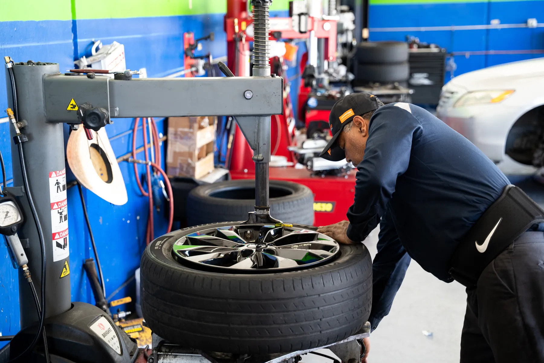 Technician leaning over a tire changer, working a tire onto a black alloy wheel